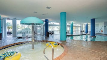 Zona de piscina interior con fuente de agua, un flotador amarillo inflable y un tobogán de agua azul.