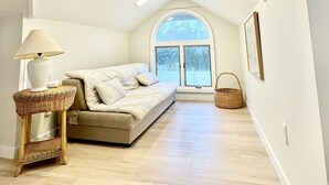 Una stanza con soffitto alto e a volta, un'ampia finestra ad arco, un divano, una lampada e un cesto.