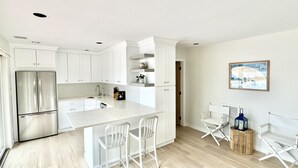 Una cucina moderna con mobili bianchi, un frigorifero in acciaio inossidabile, un piano di lavoro in marmo e una zona pranzo con sedie bianche.