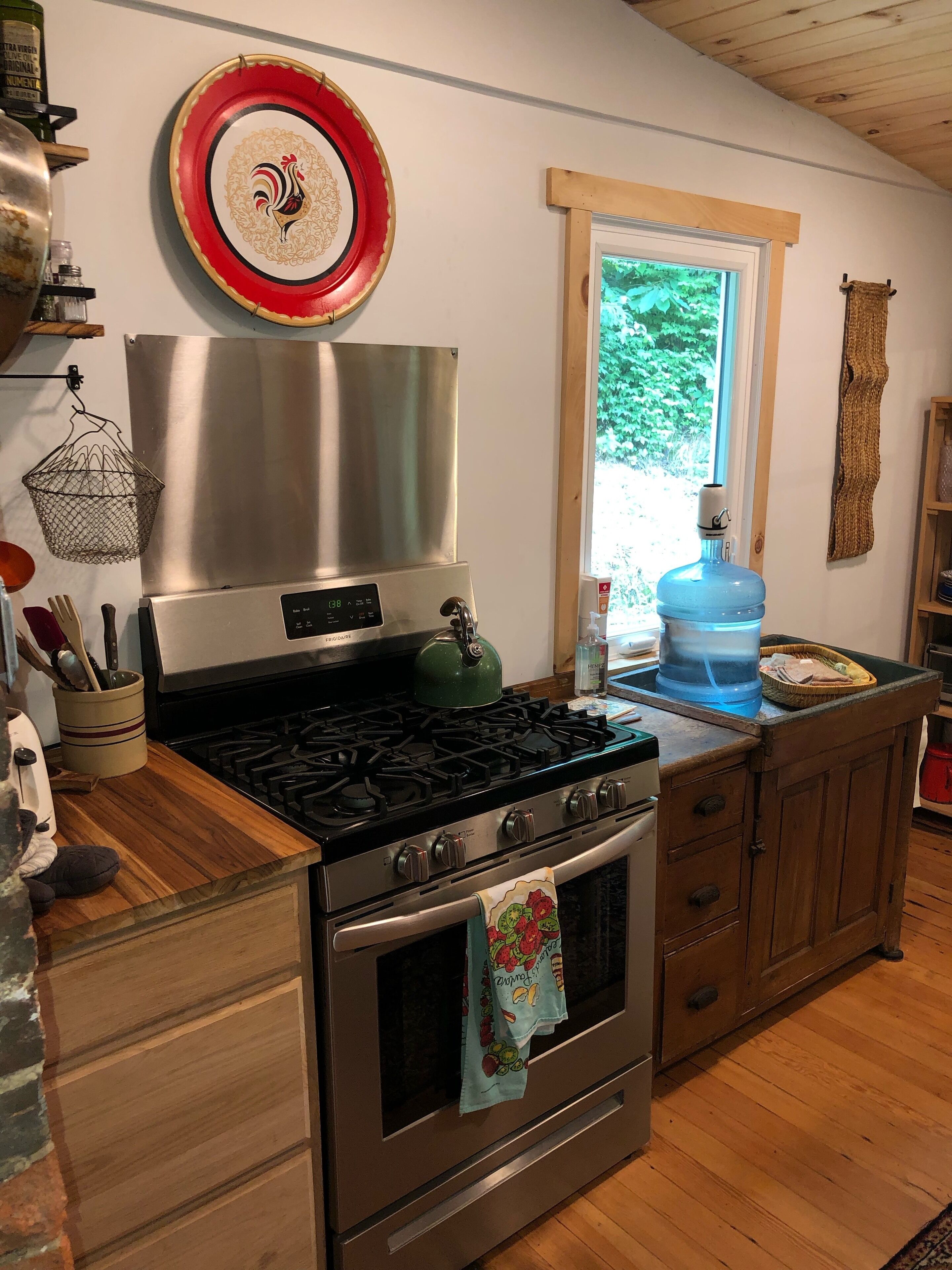 A kitchen with a stainless steel stove, wooden cabinets, a large water dispenser, and a window with a view of greenery.