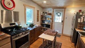 Una cocina con suelo de madera, estufa, refrigerador y una pequeña mesa con alfombra.