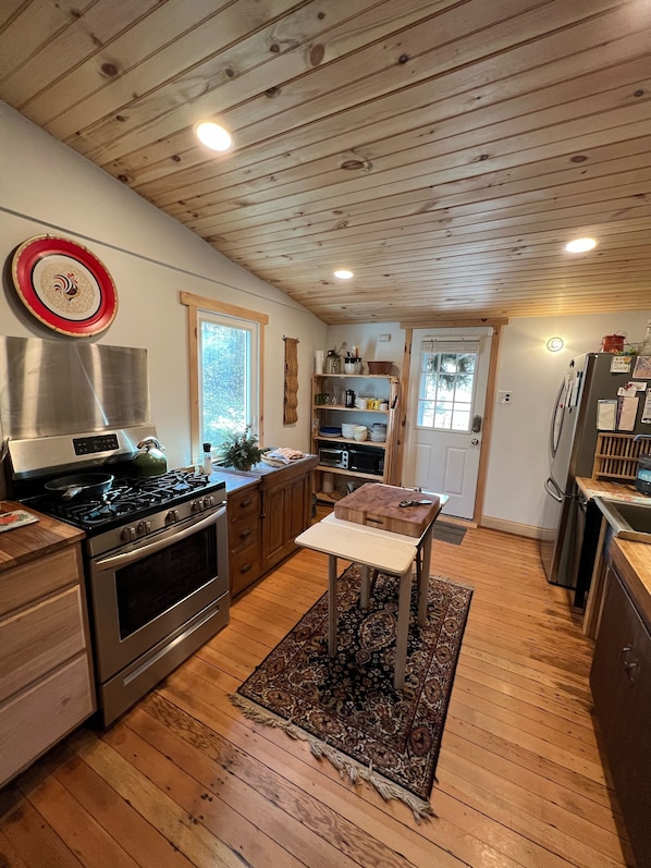 A kitchen with wooden flooring, a stove, a refrigerator, and a small table with a rug.