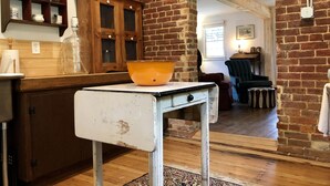 Una cocina rústica con un mueble de madera, un tazón naranja grande sobre una mesa blanca y una pared de ladrillo.