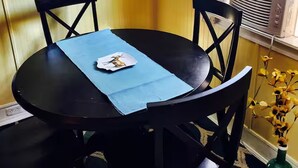 Een eethoek met een ronde tafel, vier stoelen, een blauwe placemat, een klok aan de muur en een airconditioning.