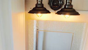 Een badkamer met een wit wastafelmeubel, twee plafondlampen en een bord boven de spiegel met daarop 'BATHROOM RULES'.