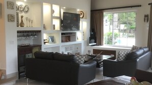 Una sala de estar moderna con un sofá negro, una mesa de comedor y un televisor. Hay un ventilador de techo y un equipo de aire acondicionado.