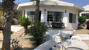 Un edificio blanco con un porche techado, ventanas amplias y mesas al aire libre.