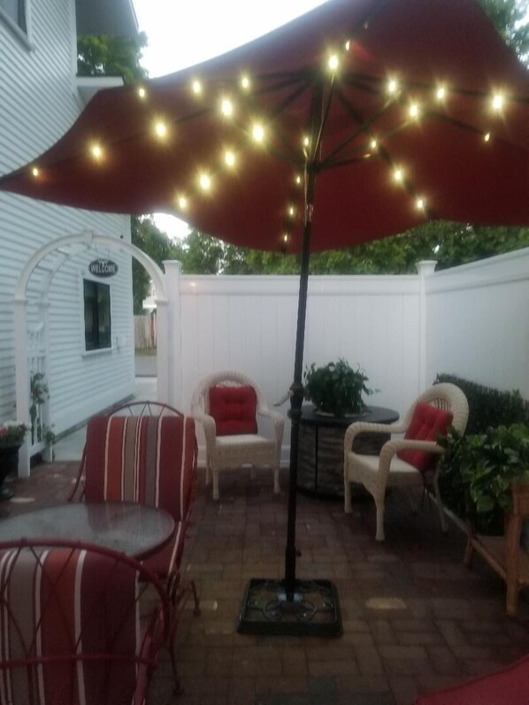 Eine Terrasse im Freien mit einem roten Sonnenschirm, Korbstühlen und einem kleinen Tisch.