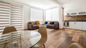 Un salon moderne avec une table à manger en verre, un canapé avec des coussins et un coin cuisine doté de placards et d’un plan de travail.