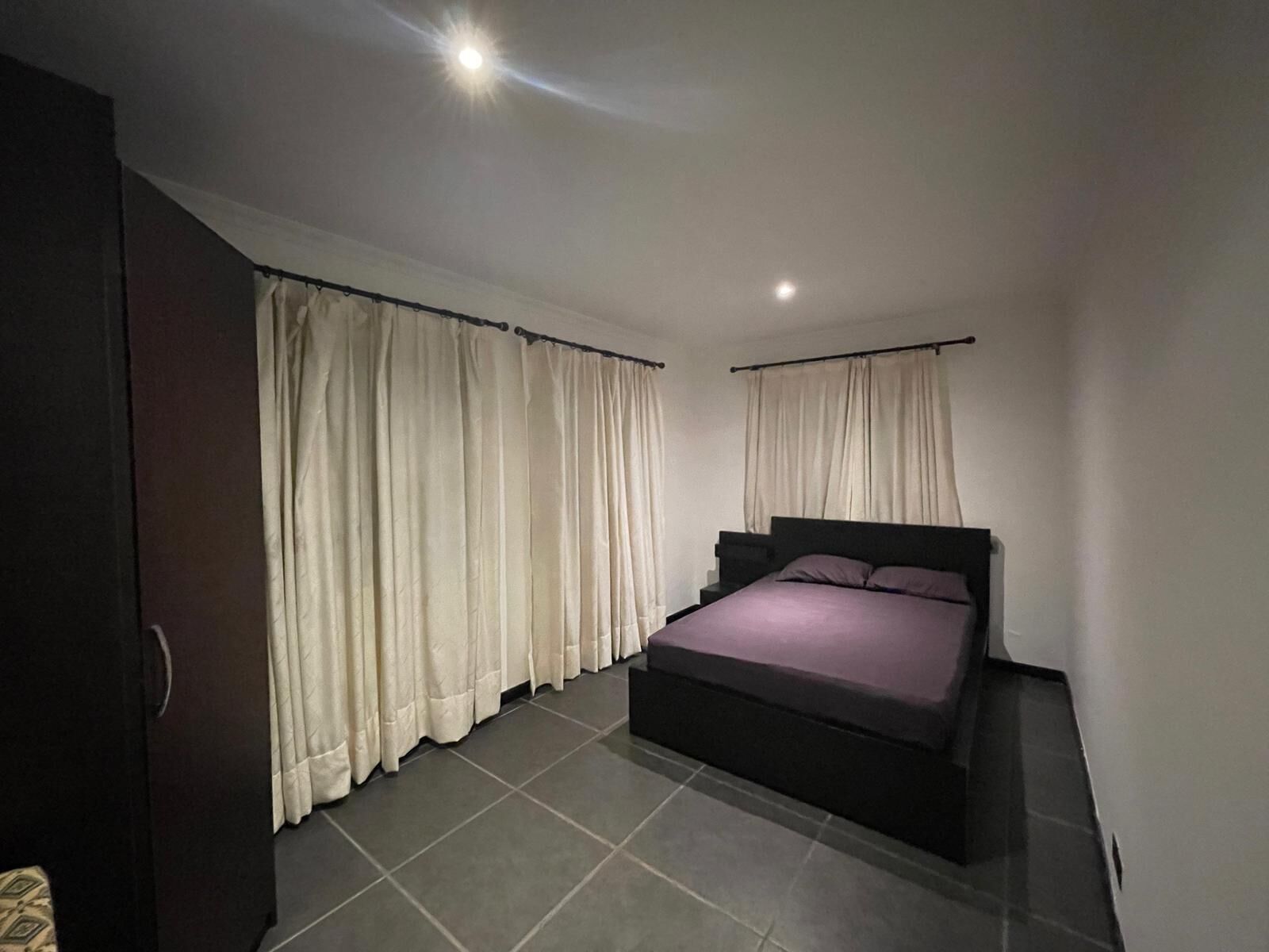 Une chambre à coucher avec un lit, des rideaux et un sol carrelé.