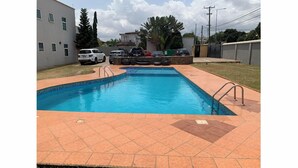 A rectangular swimming pool with a tiled deck, surrounded by a stone wall and a metal fence. - Remarkable 2-Bed Apartment in Accra (Accra)