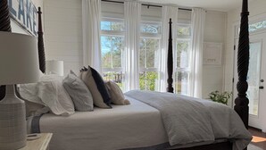 Ein Schlafzimmer mit Bett, Nachttisch, Lampe und einem Fenster mit Vorhängen.