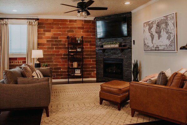 A living room with a brick wall, a fireplace, a flat-screen TV, and a world map on the wall.