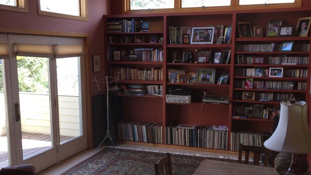 Ein Zimmer mit einem großen Bücherregal voller Bücher und gerahmten Fotos, einem Esstisch mit Stühlen und einem gemusterten Teppich.