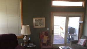Ein Wohnzimmer mit einem violetten Sessel, einem Holztisch, einem kleinen Beistelltisch mit Lampe, einem gesteppten Stuhl und einem Sofa mit gestreiftem Kissen.