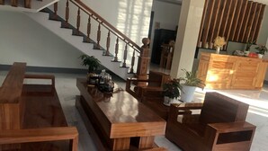Amplia sala de estar con una mesa de centro de madera, un sofá y una silla. Se ve una escalera con barandas de madera al fondo.
