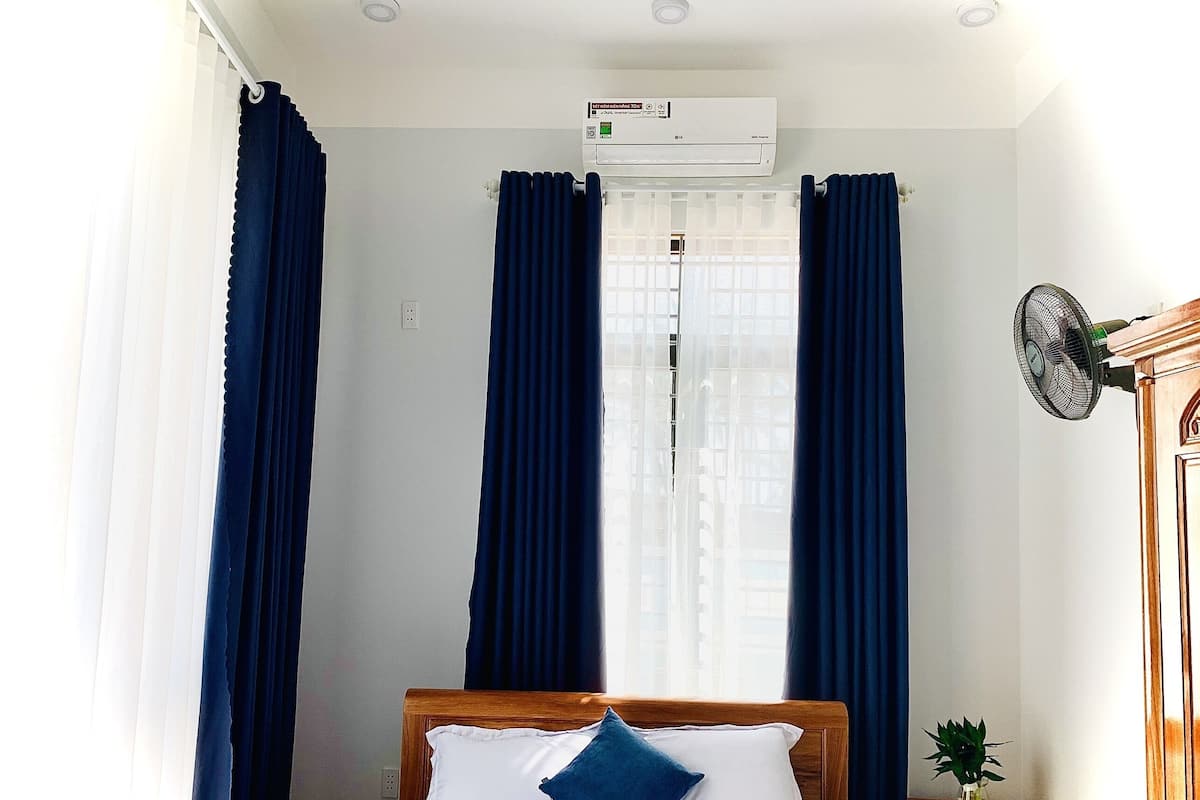 Une chambre d’hôtel équipée d’un lit, d’une table de chevet, d’un ventilateur fixé au mur et d’un appareil de climatisation.
