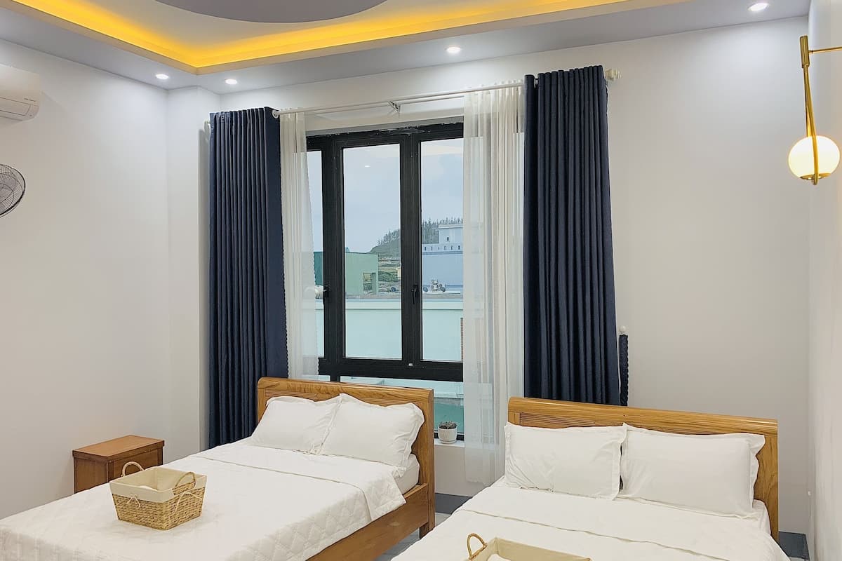 Une chambre d’hôtel avec deux lits, une fenêtre avec des rideaux, un luminaire au plafond et une petite table de chevet.