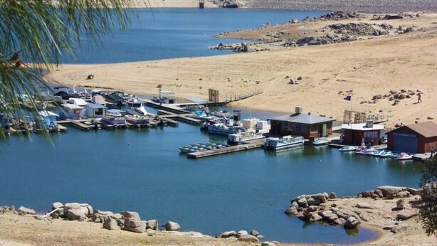 Uma marina com barcos atracados, um pequeno edifício e um litoral rochoso.