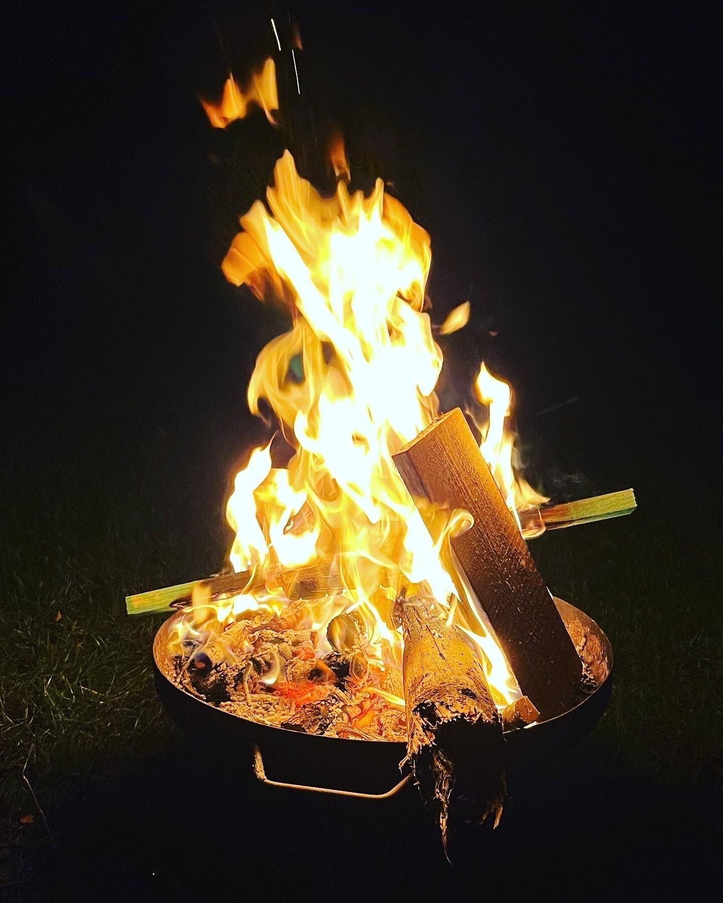 A campfire with burning wood and a metal pot.