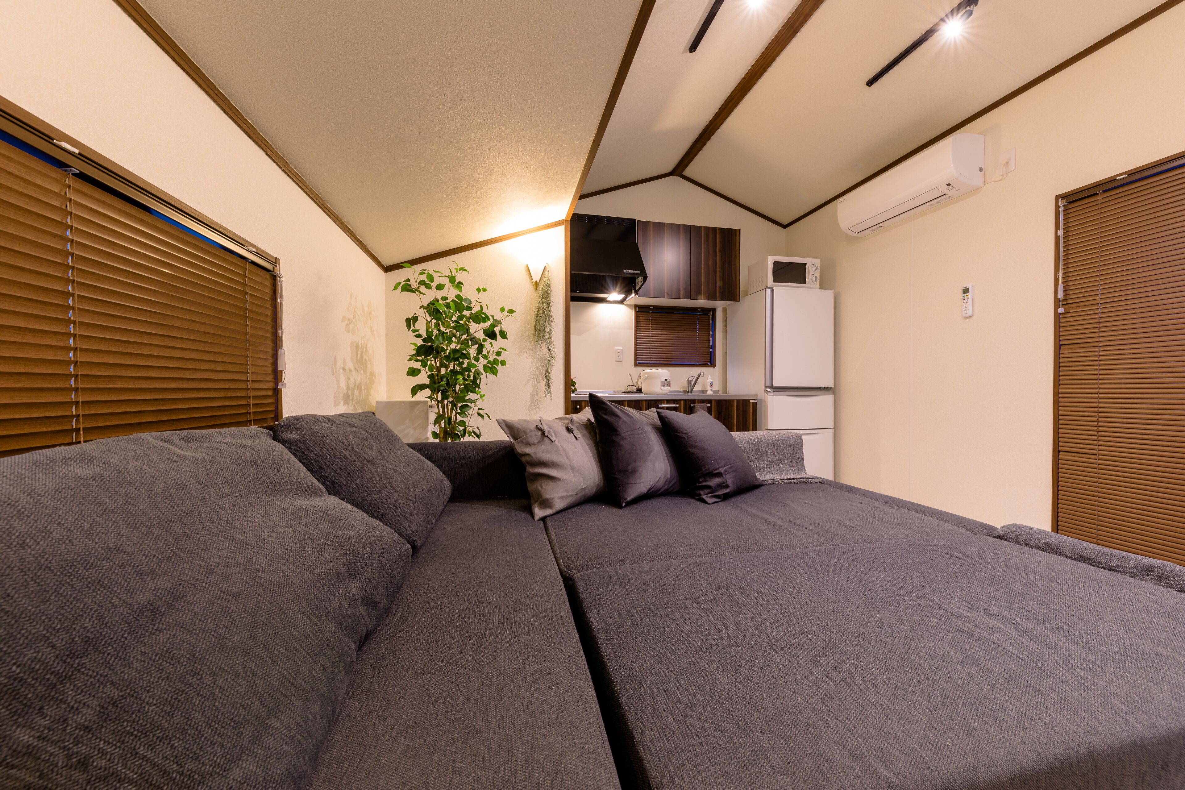 A compact living space with a sofa, a small kitchen area, and a window with blinds.