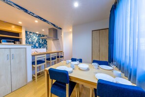 A dining area with a wooden table set for four, blue chairs, and a kitchen in the background.