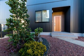 A modern building with a large window and a door. There is a garden with various plants and a rock.