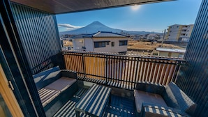 En balkon med fletningsmøbler, udsigt til et bjerg og et træhegn.