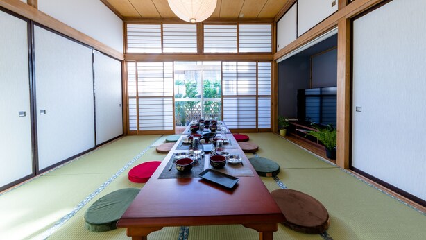 A traditional Japanese room with tatami flooring, a low wooden table set for a meal, sliding doors, and a view of greenery outside. - RAKUWA Bettei (Fujikawaguchiko)