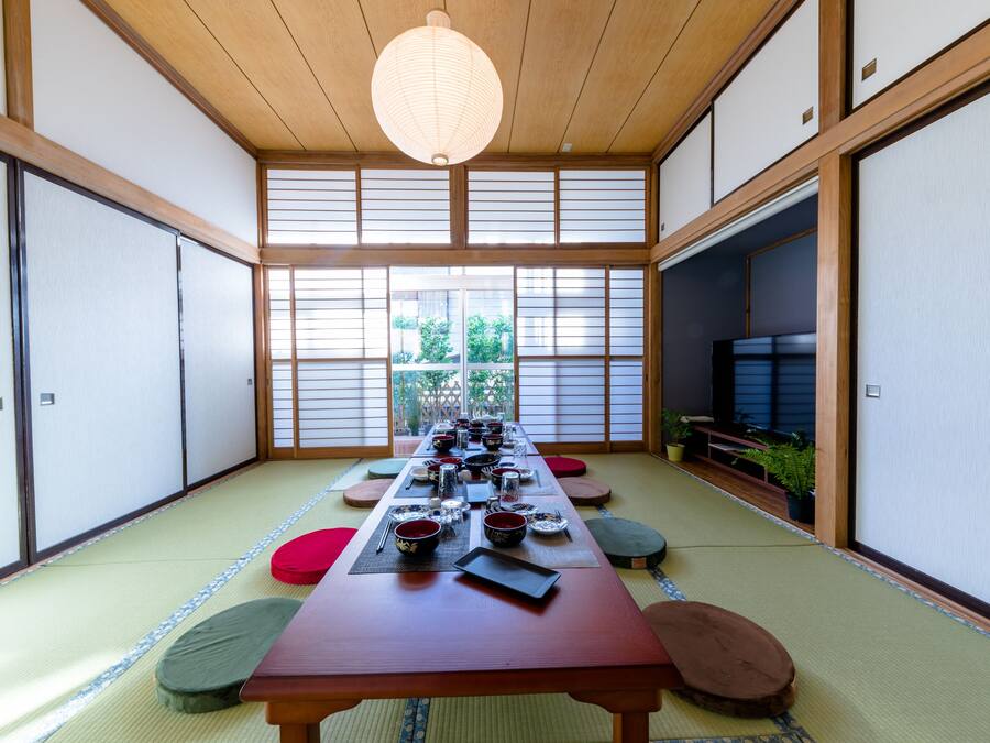 Una habitación japonesa tradicional con suelo de tatami, una mesa de madera baja dispuesta para una comida, puertas correderas y vistas a la vegetación exterior.