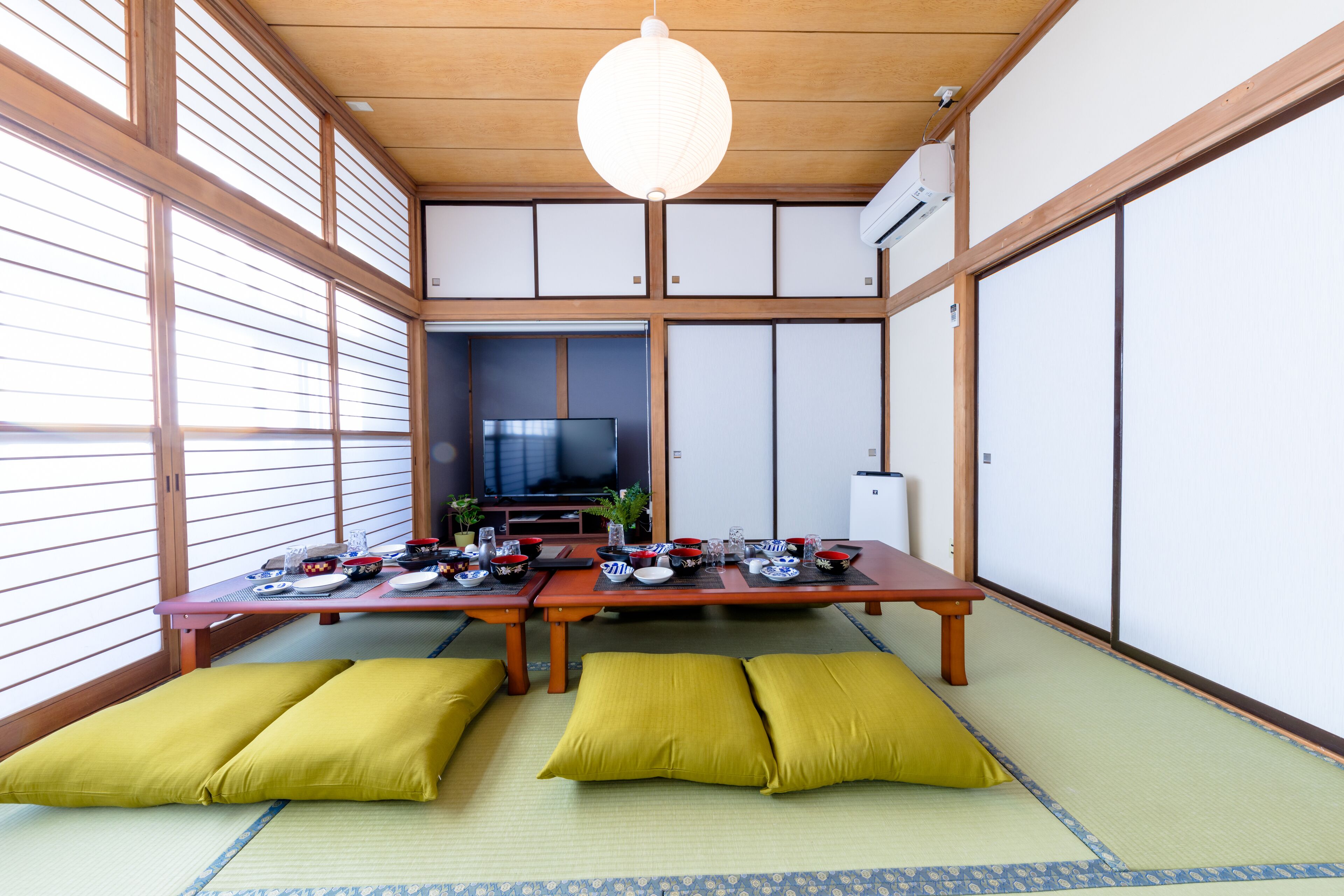 Une pièce de style japonais traditionnel, avec un sol recouvert de tatamis, une petite table basse préparée pour le repas et un téléviseur en arrière-plan.