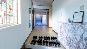 A hallway with a row of black shoes on the floor, a reception desk with a framed certificate, and a large window with a view of trees. - RAKUWA Bettei (Fujikawaguchiko)