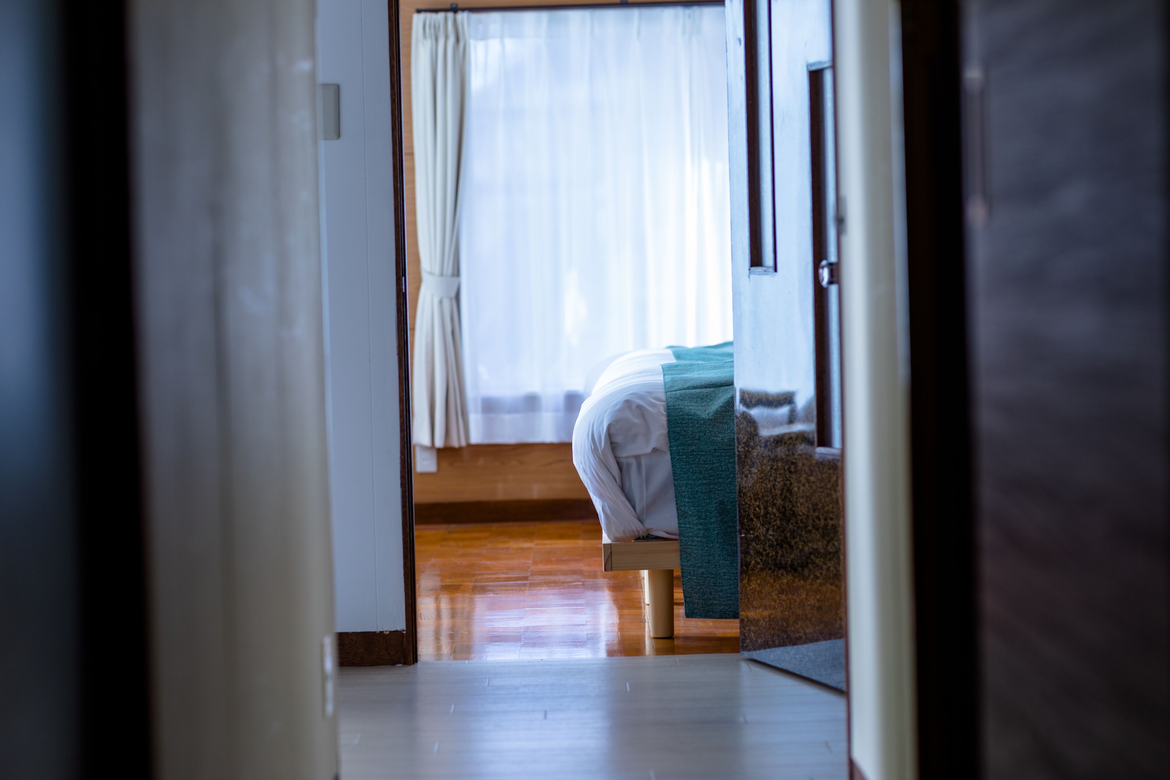 A room with a bed, a wooden floor, and a window with curtains.