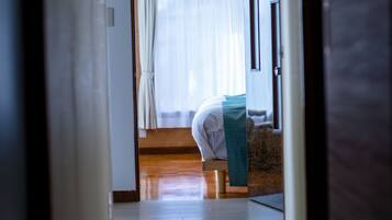 A room with a bed, a wooden floor, and a window with curtains.