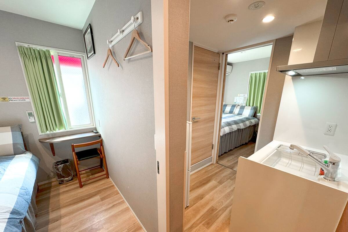 A compact hotel room with a bed, a small table, a mirror, a sink, and a window with curtains.