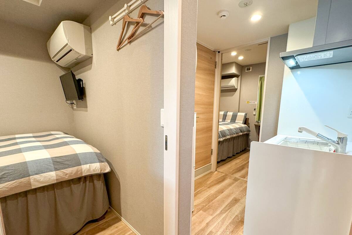 A compact hotel room with a bed, a small kitchenette, and a bathroom.