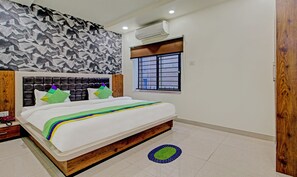 A bedroom with a bed, a patterned wall, a window with bars, and an air conditioning unit. - Treebo Golden Heights (Golmuri)
