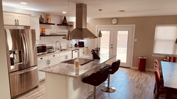 A modern kitchen with a stainless steel refrigerator, granite countertops, and a central island with bar stools.