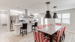 A modern kitchen with stainless steel appliances, a central island, and a dining area with striped chairs.
