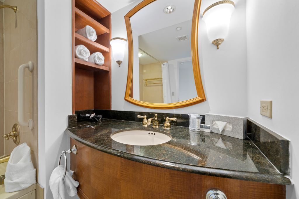 A bathroom with a marble sink, wooden vanity, and a large mirror.