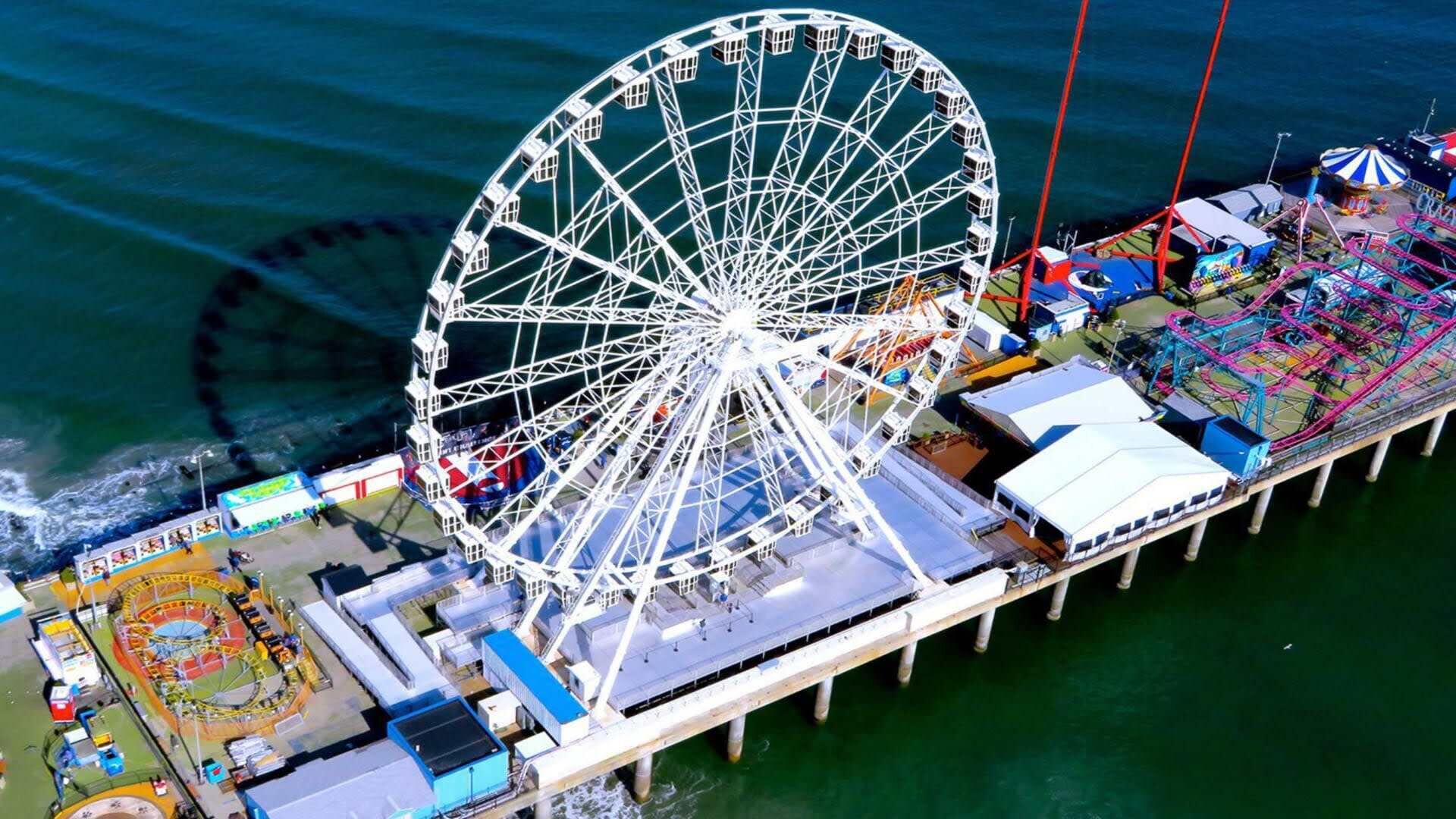 A pier with a large Ferris wheel, a carousel, and various amusement rides.