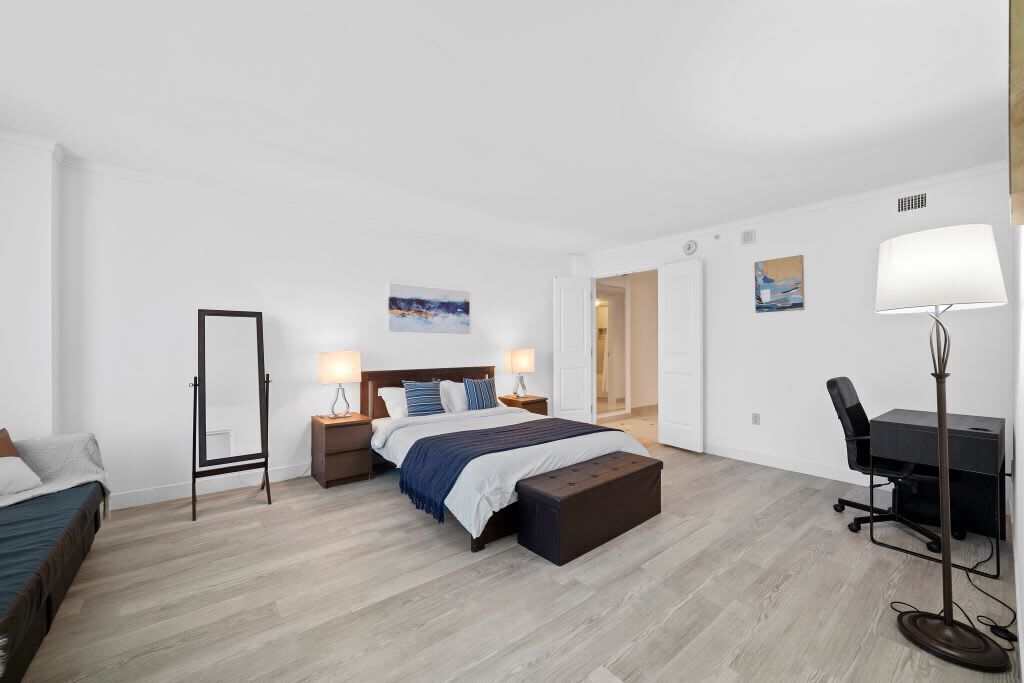Une chambre à coucher moderne avec un lit, des tables de chevet, un bureau et une lampe sur pied.