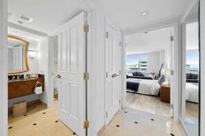 A hotel room with a large bed, a bathroom with a mirror and vanity, and a view of the city. - 2BR 3BA Ocean Front condo on the Boardwalk | CozySuites (Atlantic City)