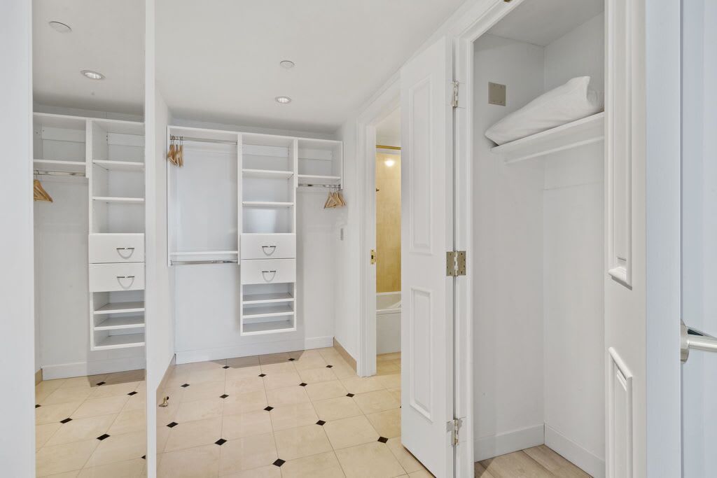 Un grand dressing avec de nombreuses étagères et tiroirs, un sol carrelé et une porte blanche donnant sur une autre pièce.
