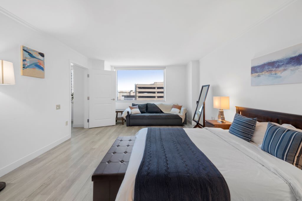 A modern hotel room with a large bed, a desk, and a view of the cityscape.