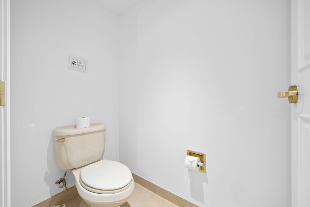 Et lille, hvidt badeværelse med toilet, gylden skylleknap og hvid toiletpapirholder.