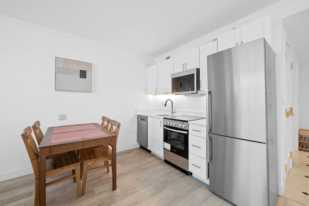 Una cocina compacta con armarios blancos, un refrigerador de acero inoxidable, un microondas y un lavavajillas.
