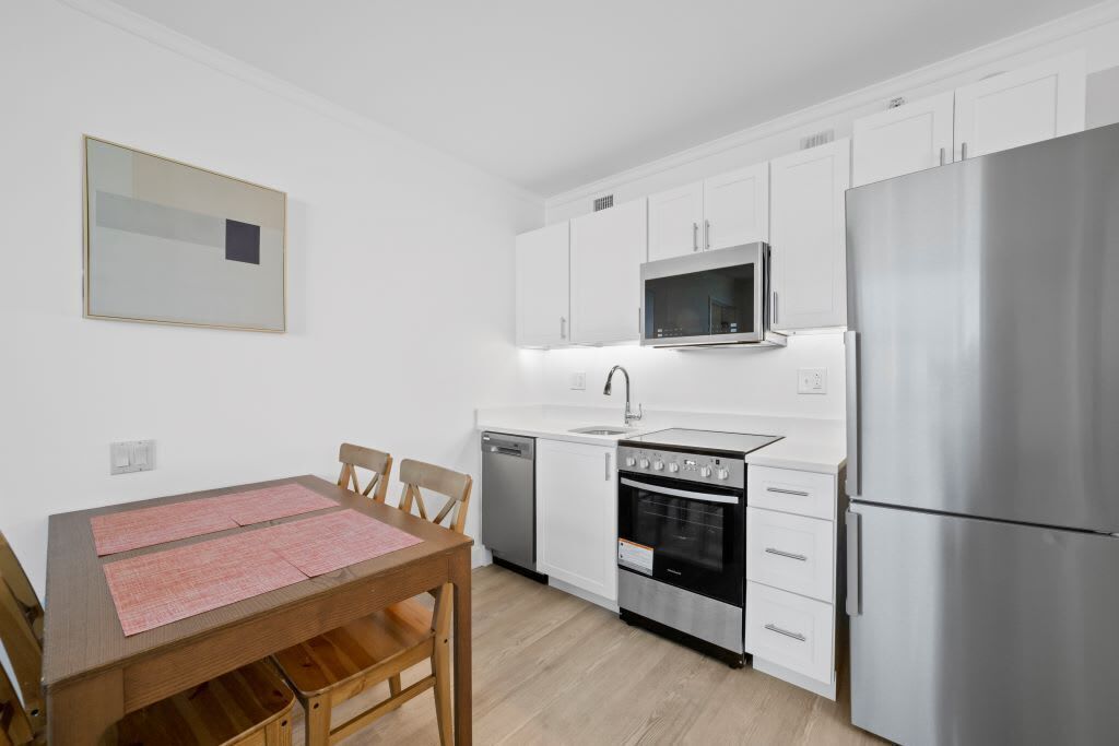 Una cocina compacta con armarios blancos, un refrigerador de acero inoxidable, un microondas, un horno y un lavavajillas.