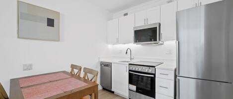 Una cocina compacta con armarios blancos, un refrigerador de acero inoxidable, un microondas, un horno y un lavavajillas.