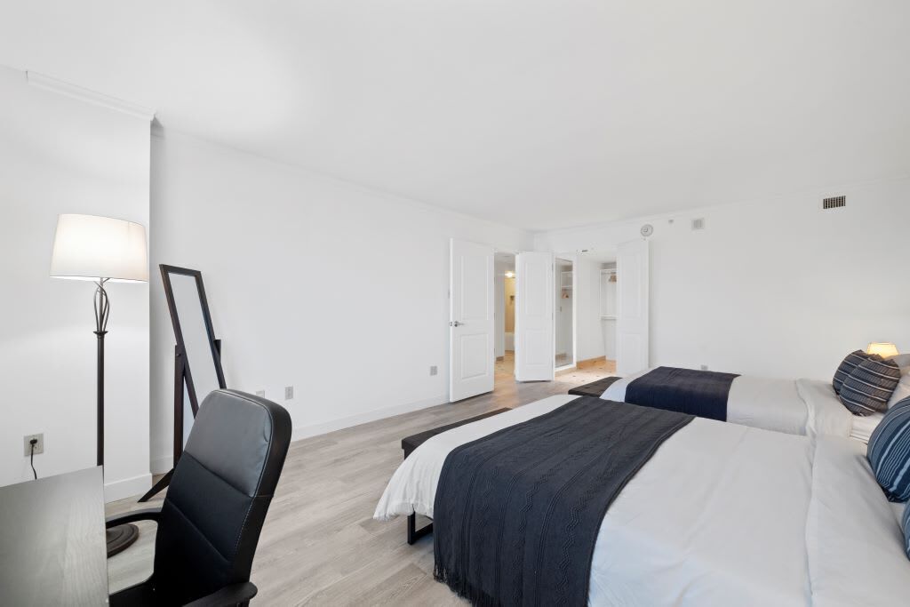 A hotel room with a bed, a desk, a chair, and a lamp.